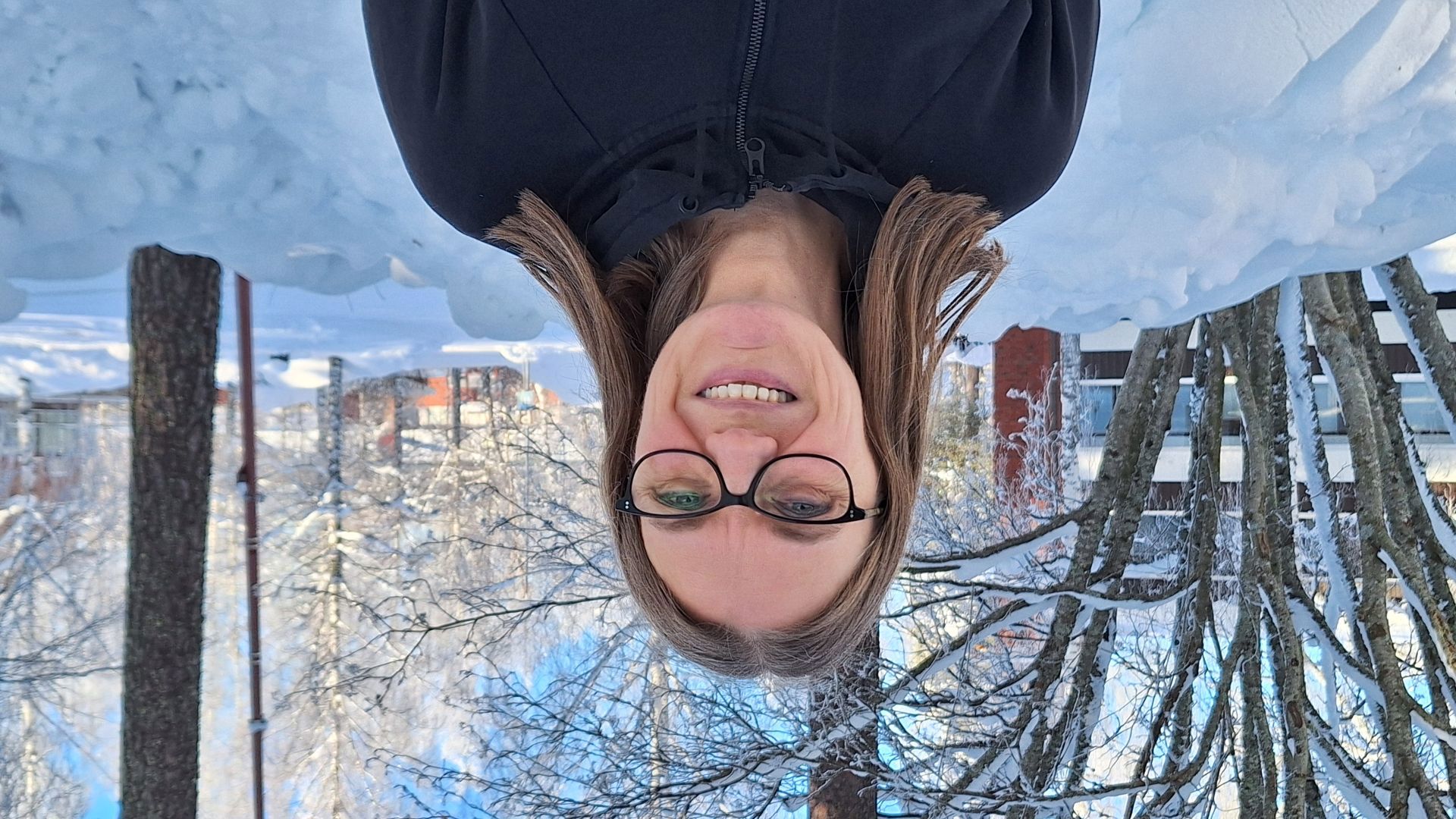 Hymyilevä silmälasipäinen naishenkilö puolilähikuvassa, kuvattu talvella ulkona.