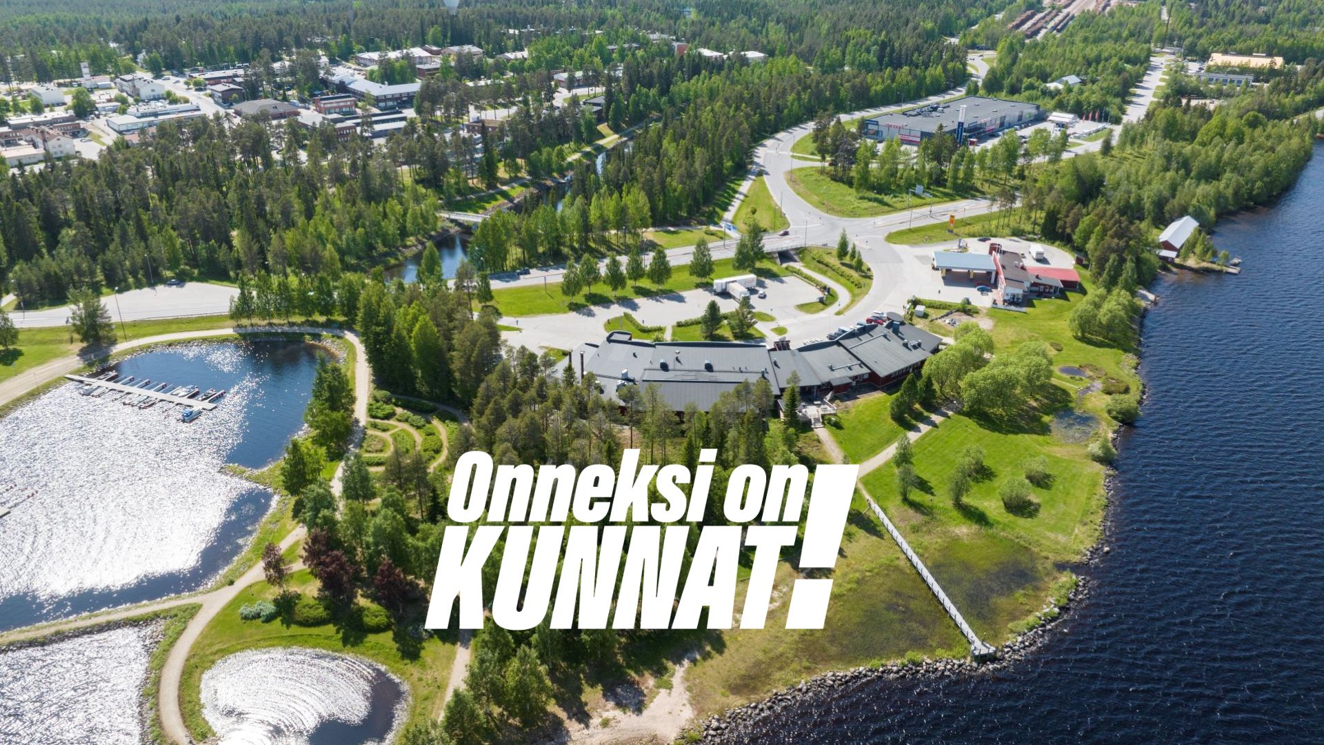 Kuvituskuvassa kesällä otettu ilmakuva Suomussalmen keskustan ja Jalonniemen alueesta, päättä Onneksi on kunnat! -kampanjan logo.