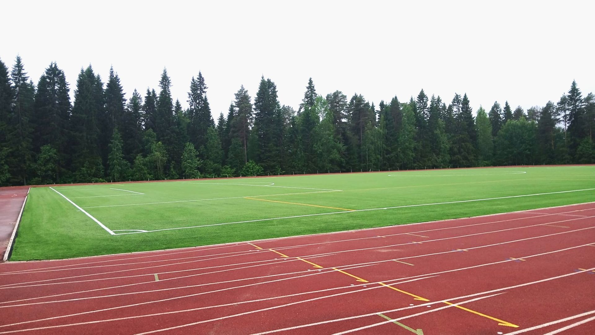 Etualalla juoksuratoja, niiden takana uusi tekonurmikenttä, joka rajautuu metsään.