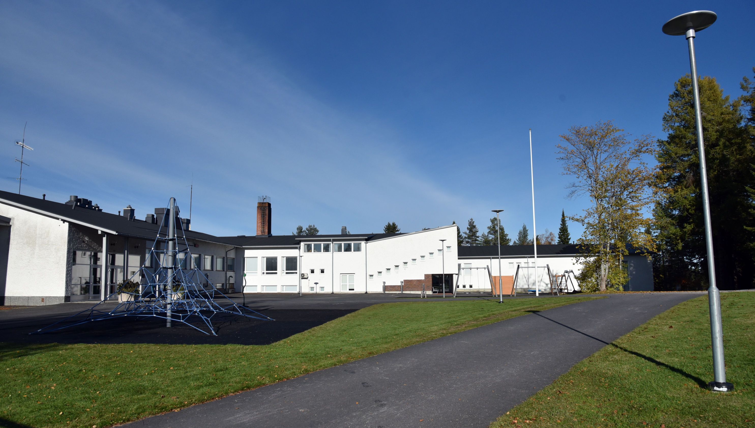 Valkoinen koulurakennus, sininen taivas ja vihreä nurmikko edessä.