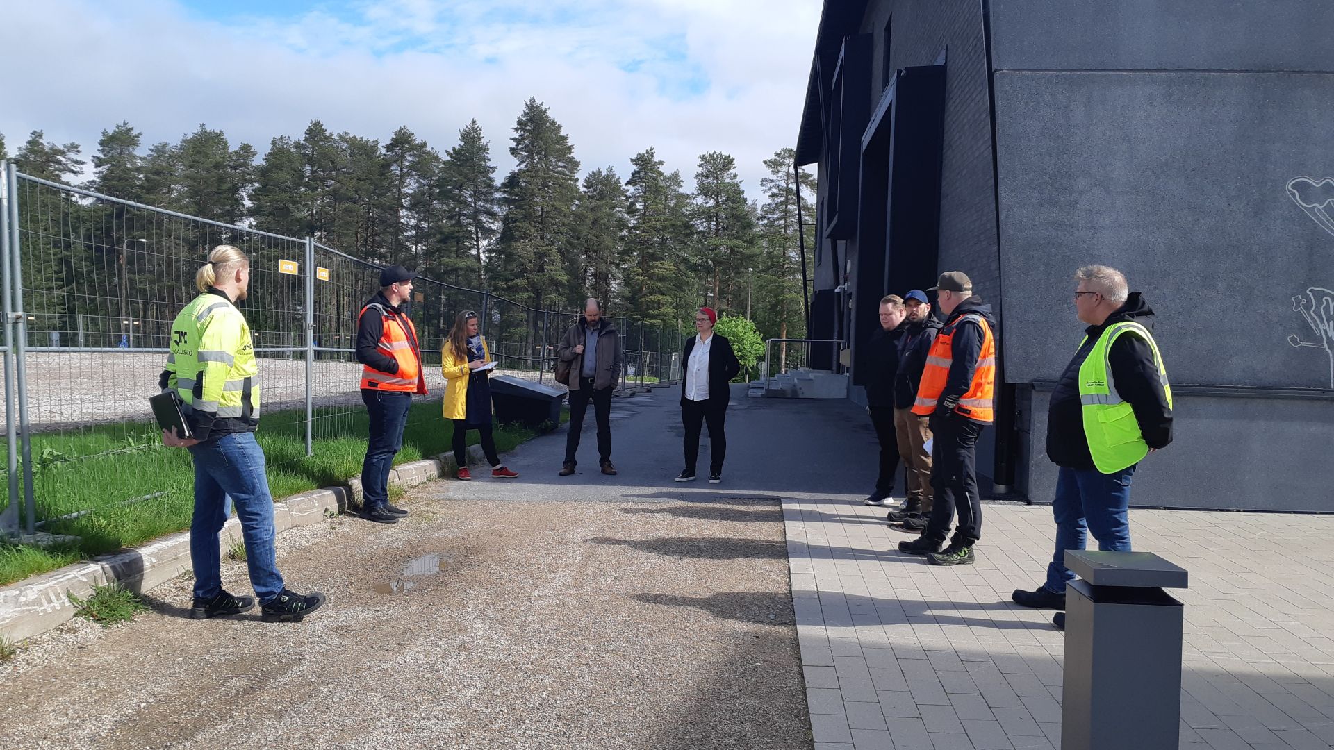 Ulkona kymmenkunta huomioliiveihin pukeutunutta henkilöä seisoo puolikaaressa.