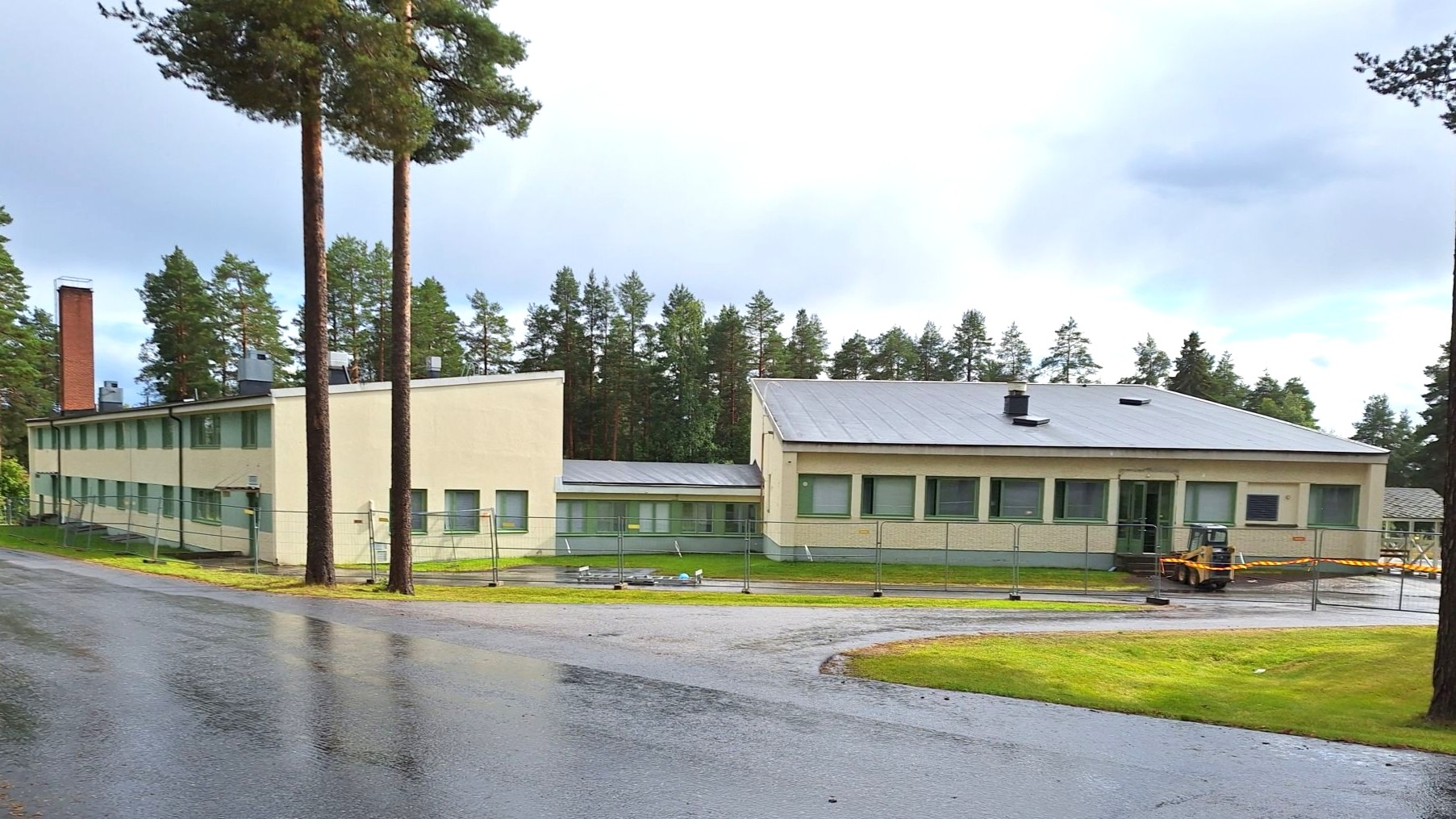 Matala 60-lukulainen koulurakennus ulkoa päin, etualalla sateesta märkää katualuetta.