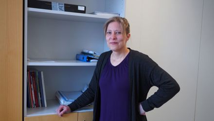 Puolilähikuvassa tummaan paitaan pukeutunut henkilö seisoo puolityhjän hyllyn luona.