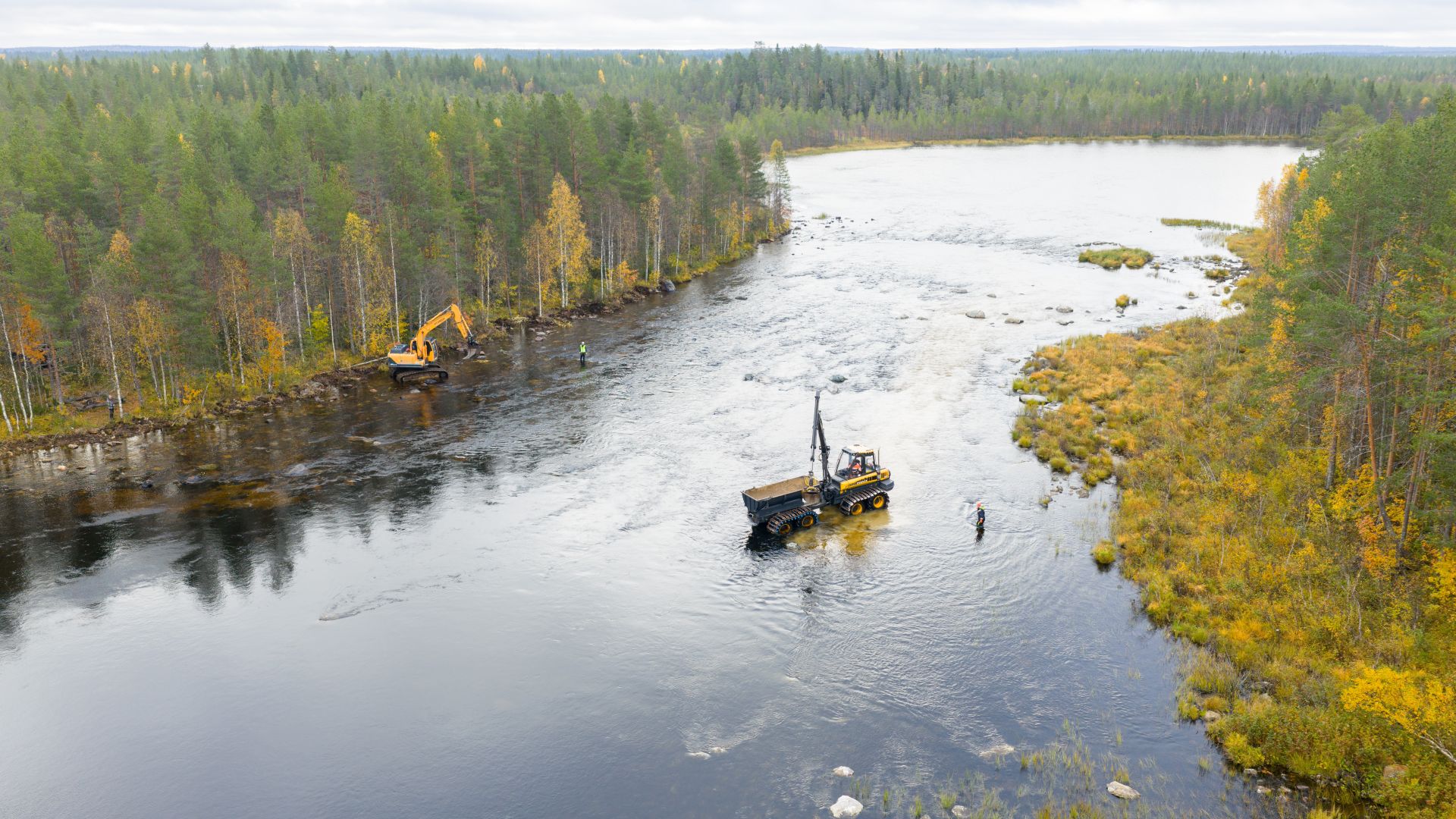 Kuvituskuvassa joki jossa työkone, kaivinkone on rannassa, metsä ympärillä on syksyinen.