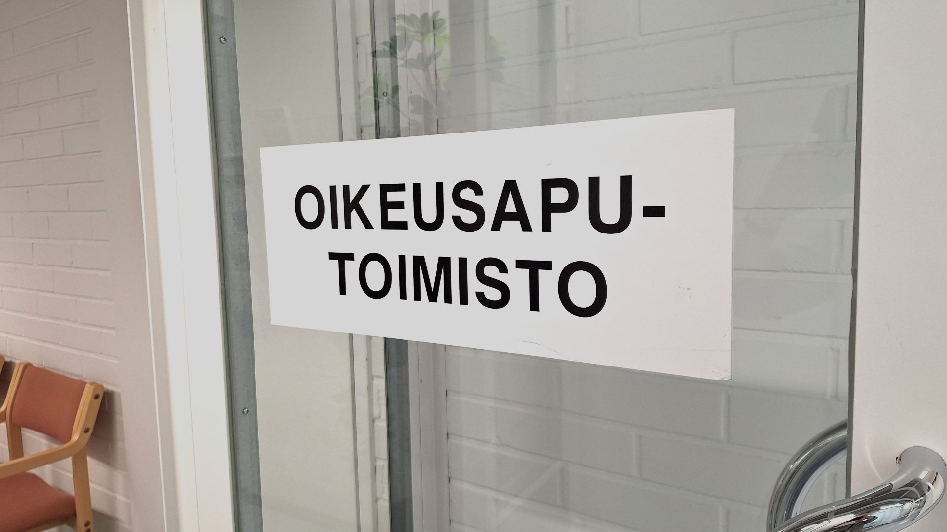 Kuvituskuvassa auki oleva lasi-ikkunainen väliovi, johon on kiinnitetty kyltti, jossa lukee oikeusaputoimisto.